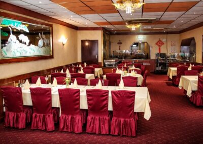 Interieur van Chinees Indisch Restaurant China in Doesburg, met rood tapijt, gedekte tafels met witte tafelkleden, rode stoelhoezen, en decoratieve elementen zoals een schilderij met kraanvogels en traditionele Chinese ornamenten.